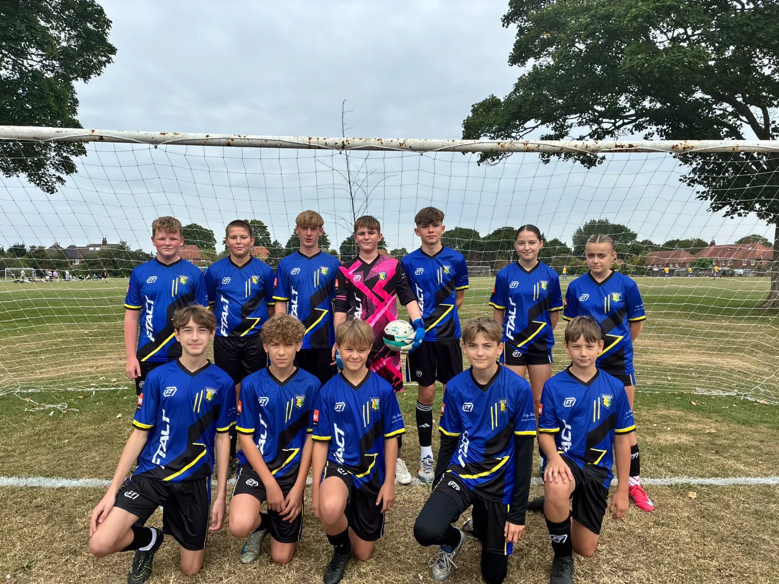 Mixed youth team in blue and black FTACT kit in front of a goal